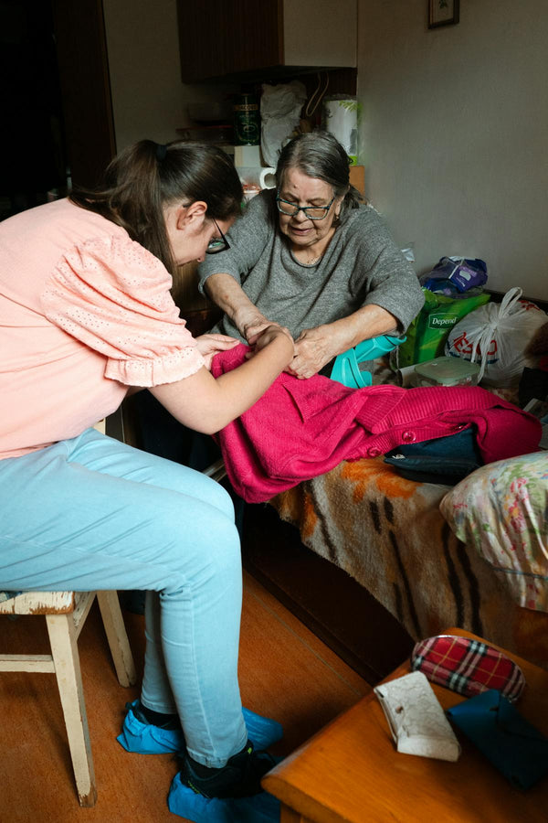 Caregiver helping elderly woman with fine motor tasks — adaptive clothing for Parkinson’s