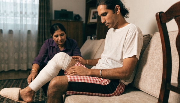 Indian man with bandaged knee in adaptive side-opening recovery shorts at home after knee replacement surgery