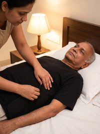 [bedridden] Caregiver with bare hands helping elderly Indian man lying in bed put on black side-opening T-shirt, hidden velcro panel pressed closed, 3:4 portrait
